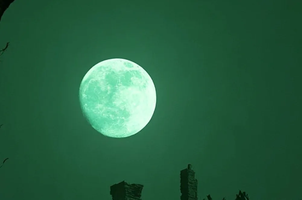 A full pale-green moon over bare black branches in a green-lit sky